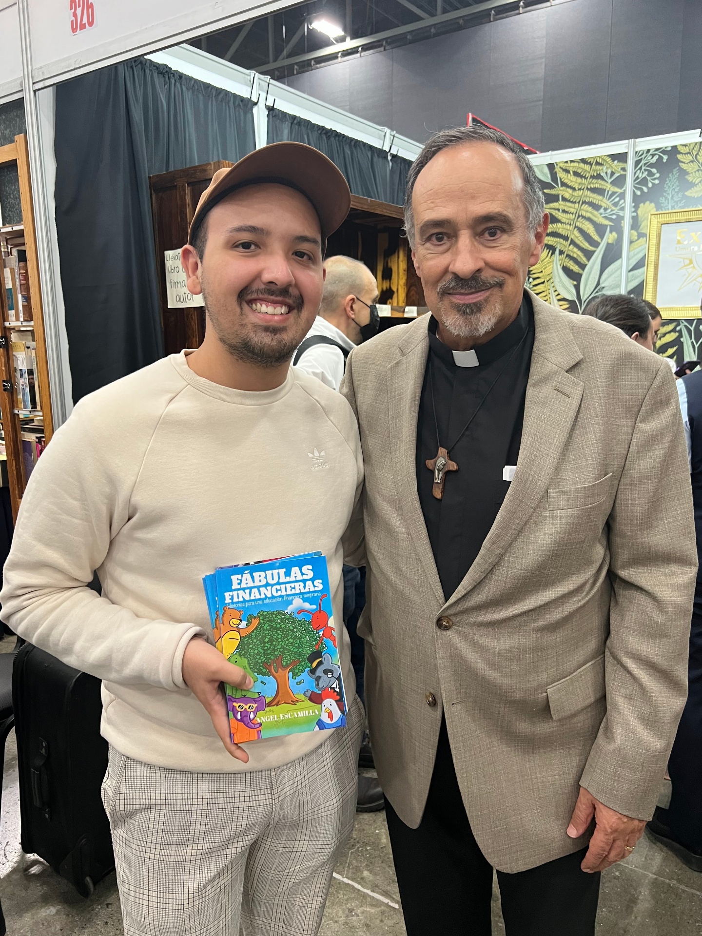 Angel Escamilla junto al Padre Ernesto Caro sosteniendo el libro Fábulas Financieras