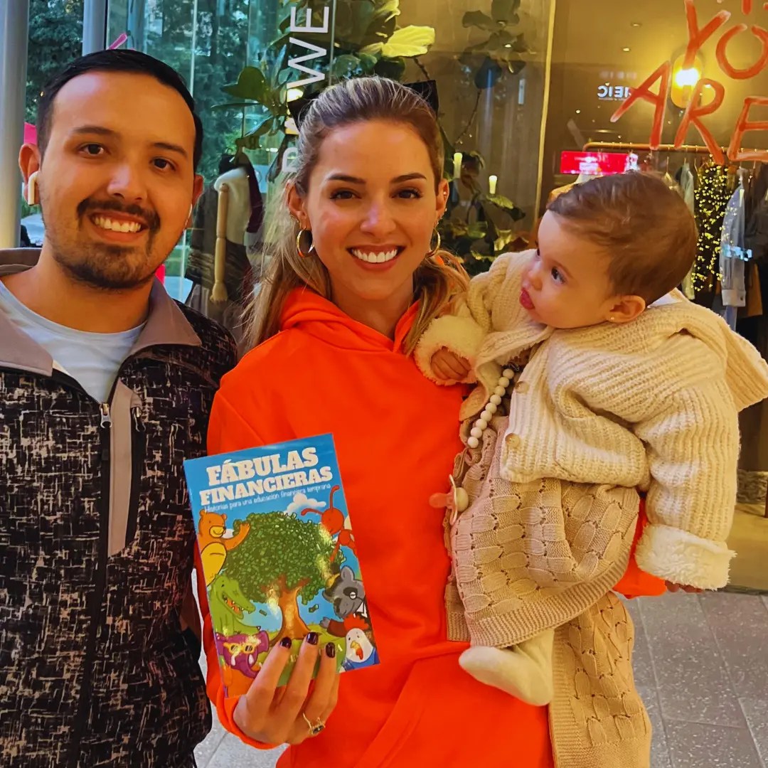 Angel Escamilla y Mariana Rodríguez Cantú sostienen el libro Fábulas Financieras junto a su hija Mariel García Rodríguez, promoviendo la educación financiera infantil.